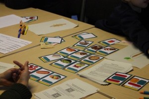 Coloured playing cards, paper and pens on a table with hands in foreground